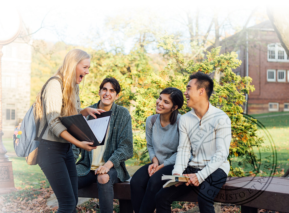 Geneva students sitting on a bench laughing together