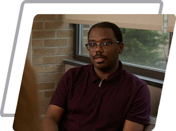 A man in a maroon shirt sits on a couch against a window, in a counseling session.